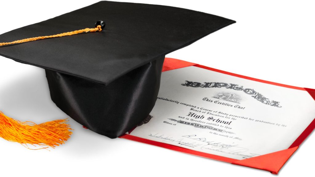 copy of high school diploma on a table next to a graduation cap with yellow gold tassel