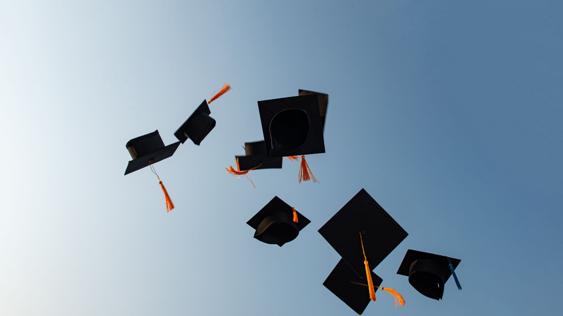 graduate caps tossing in the air behind beautiful blue sky